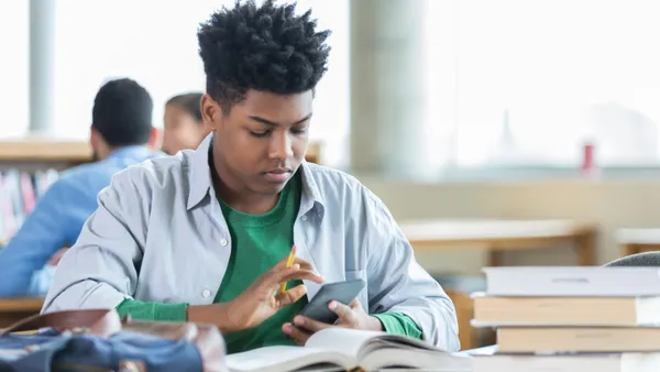 A high school student holds a calculator while completing an assignment in class.