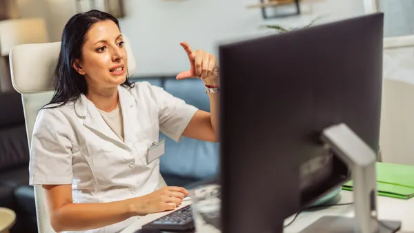 A woman sitting at her desk and using sign language to consult with a patient online.