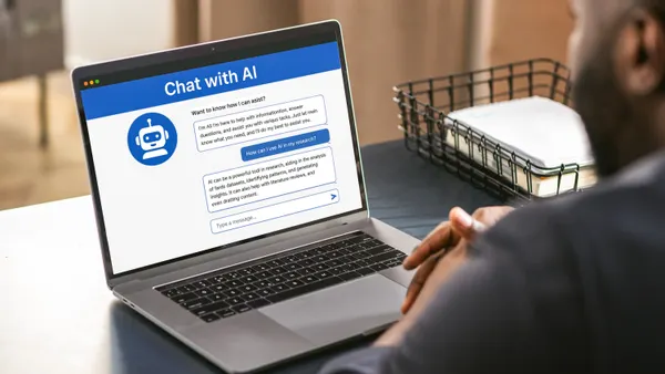 A man sits in front of a computer laptop with an AI chatbot icon on its screen.