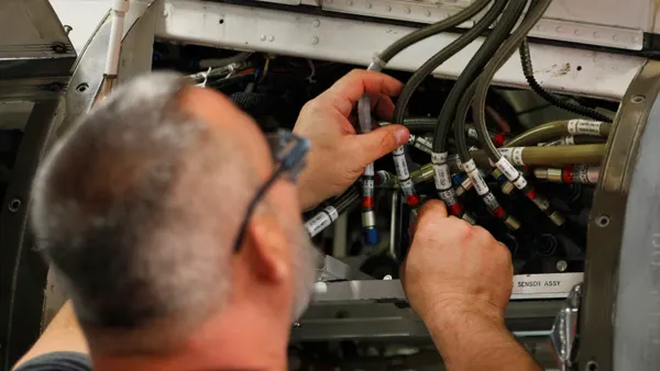 Seen from the back, a man examines a number of tubes leading into the belly of a small aircraft.