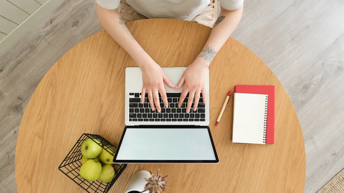 Overhead shot of a laptop near notebooks with tattooed arms typing