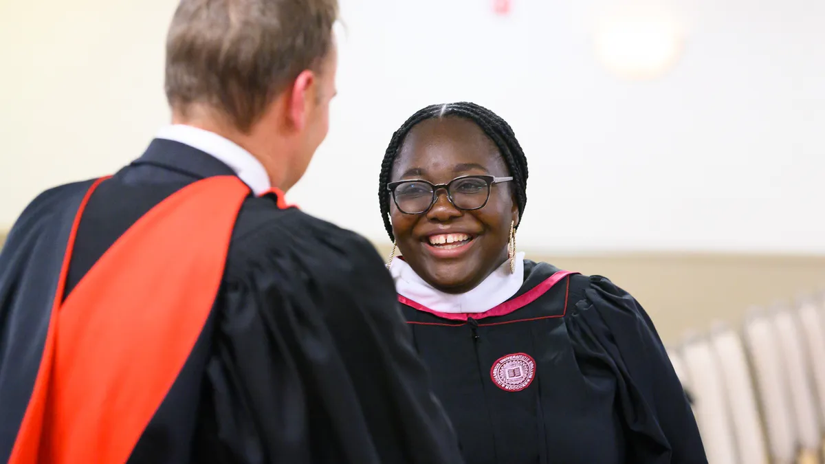 A college graduate shaking hands with the Dean and smiling at a graduation ceremony