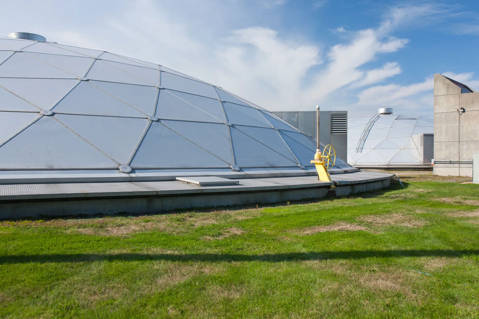 A domed structure on a grassy field on a partly cloudy day with other structures nearby.