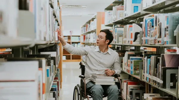 An Asian person in a wheelchair wheels through a library