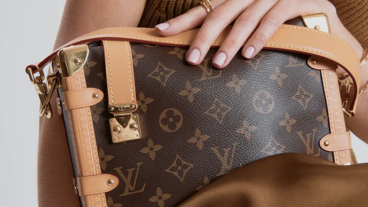 A person holds a Louis Vuitton handbag in a close-up view.