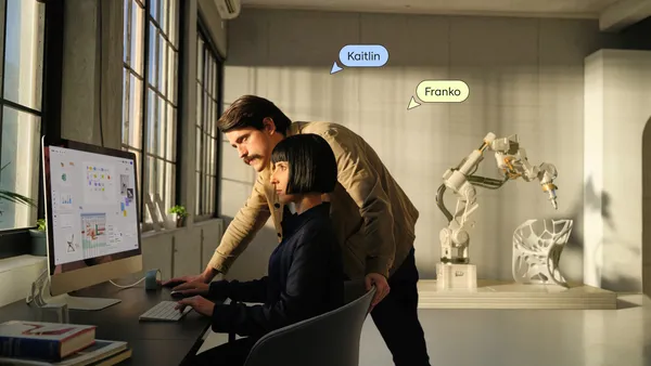 Two people by a table at an office looking at a computer.