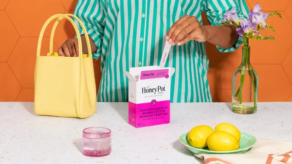 A person wearing a green striped shirt taking a tampon out of box and placing it in a yellow purse.