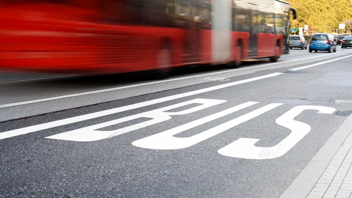 A blurred bus drives down a city street next to a bus lane.