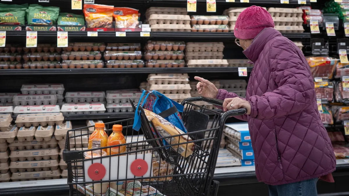 A shopper in a pink coat stands with her cart and considers the egg selection.