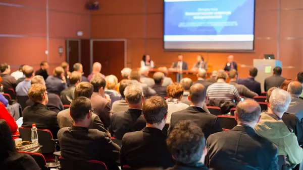 Conference attendees listen to a session in a convention center meeting room.
