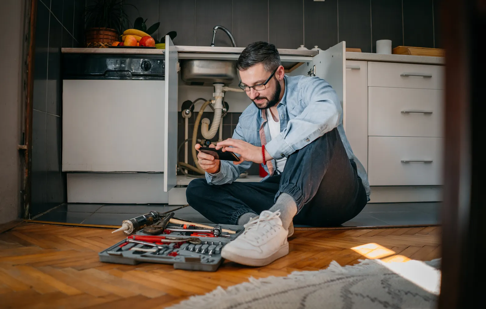 A man looks at his phone while repairing a sink.