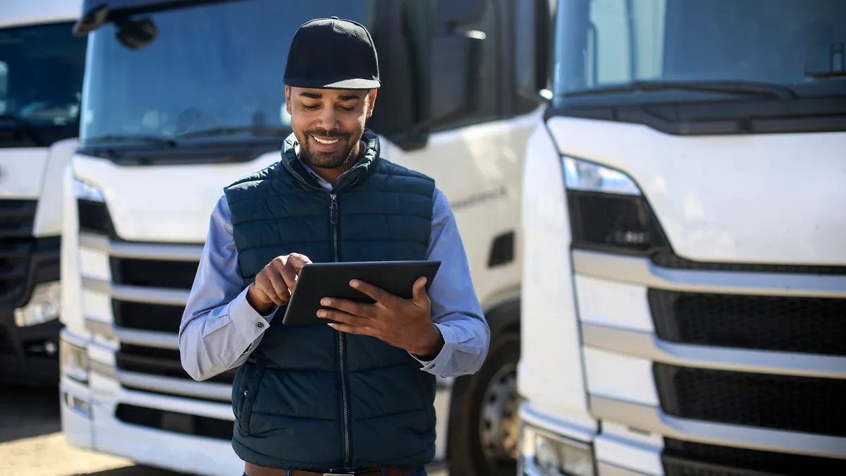 A person uses a tablet near parked trucks.