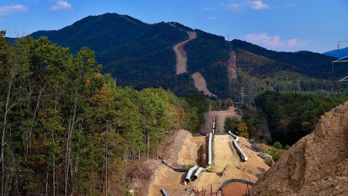 Lengths of large pipe stretch from the forest in the foreground into the mountains in the background.