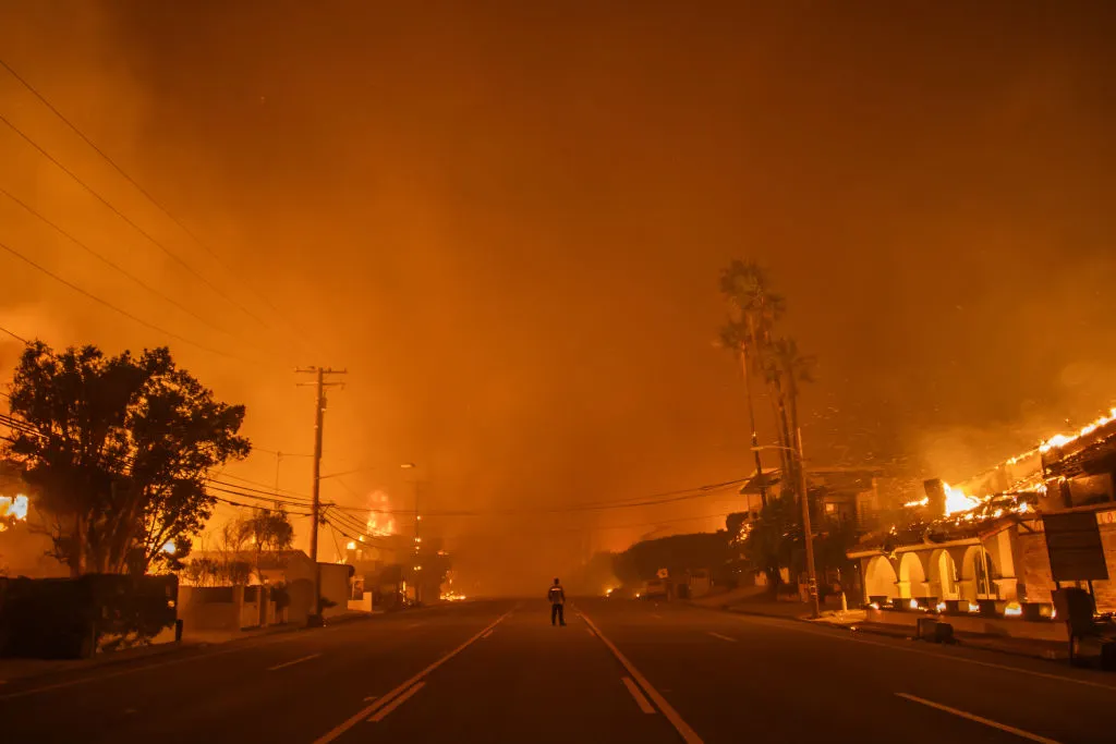 A man watches the flames from the Palisades Fire burning homes on the Pacific Coast Highway amid a powerful windstorm on Jan. 8, 2025 in Los Angeles, California.