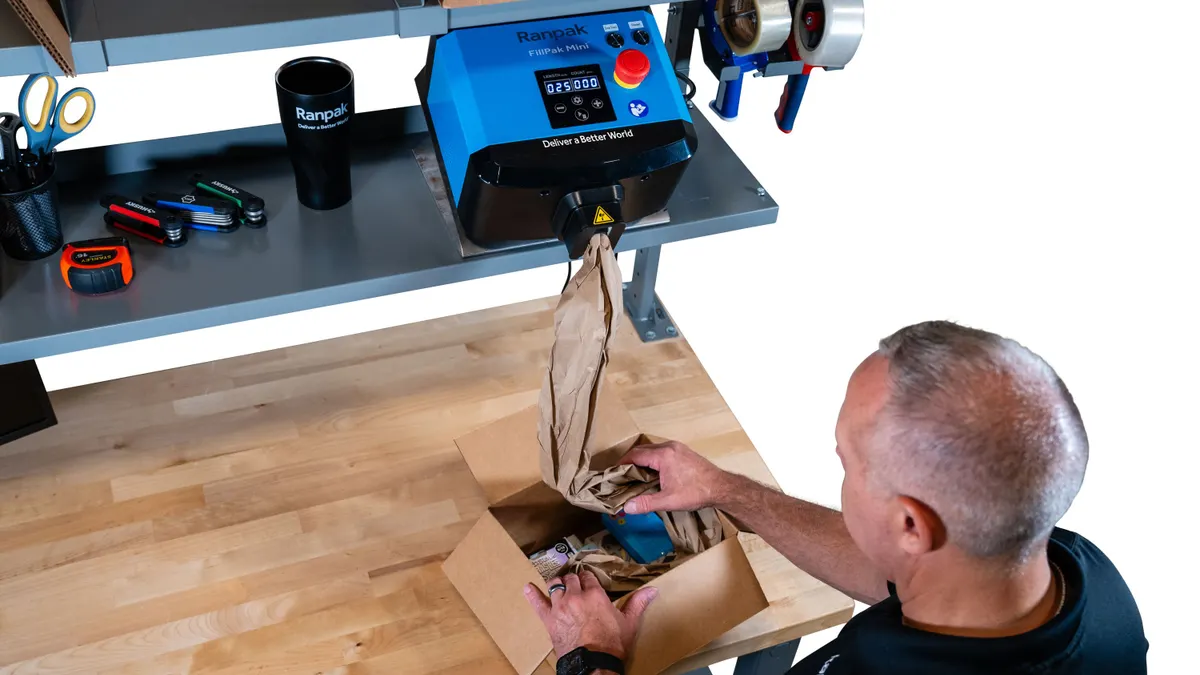 A person adds void fill to a box package using Ranpak's FillPak Mini void fill converter