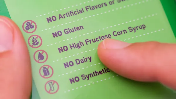 Person reading a label with the words No Artificial Flavors or Sweeteners, No gluten, No high fructose corn syrup, No dairy, No synthetics.