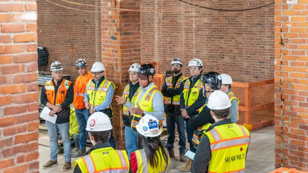 A group of workers in safety gear stand around a jobsite and talk.
