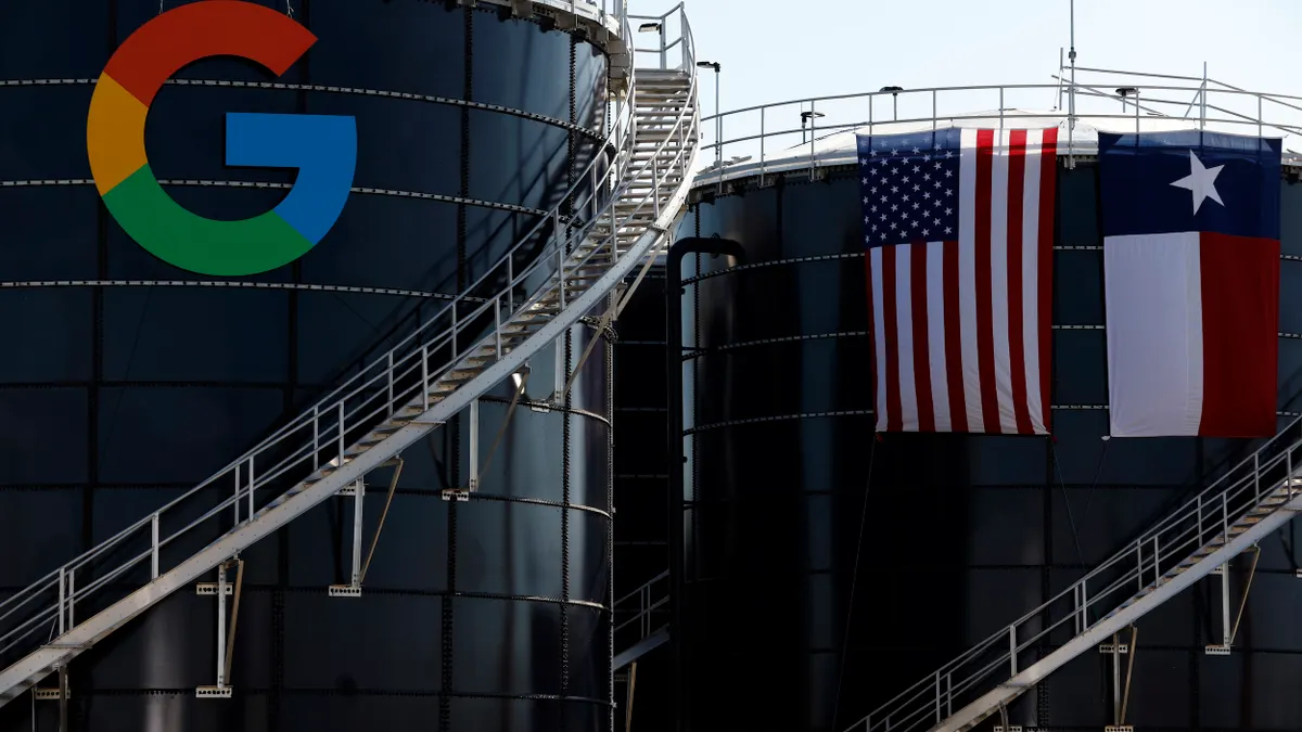 A round building with a large G and more buildings behind a U.S. and a Texas flag.