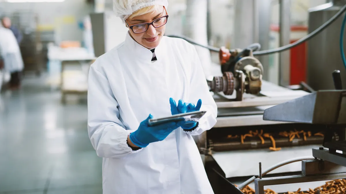 Young female worker in sterile clothes is checking quality of products in food factory.