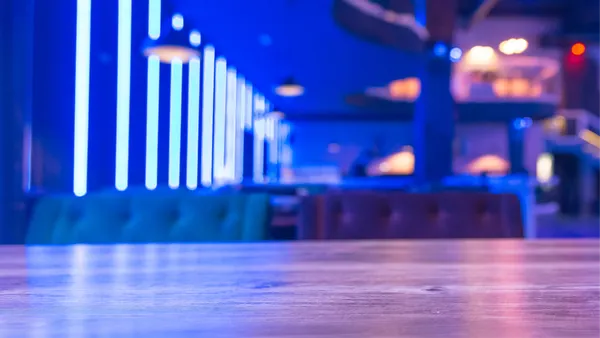 modern restaurant interior with blue neon lighting, cushioned booth seating, and a wooden tabletop in sharp focus in the foreground.