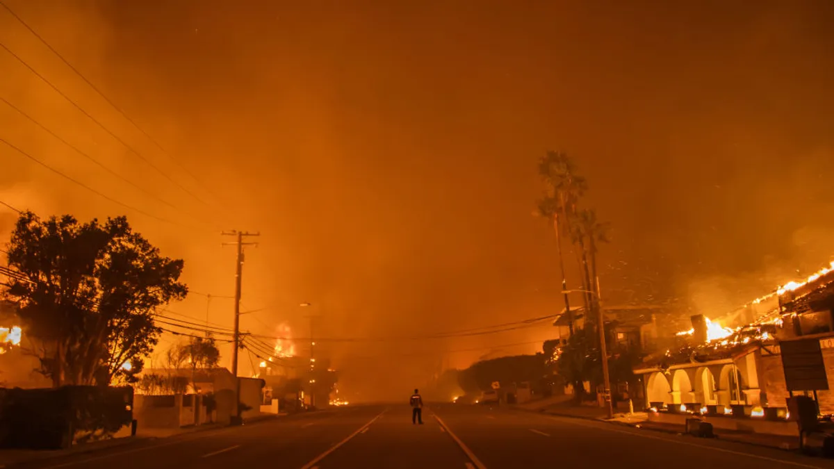 A man watches the flames from the Palisades Fire burning homes on the Pacific Coast Highway amid a powerful windstorm on Jan. 8, 2025 in Los Angeles, California.