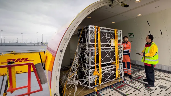 Cargo is being loaded onto an aircraft with two employees standing inside the plane.