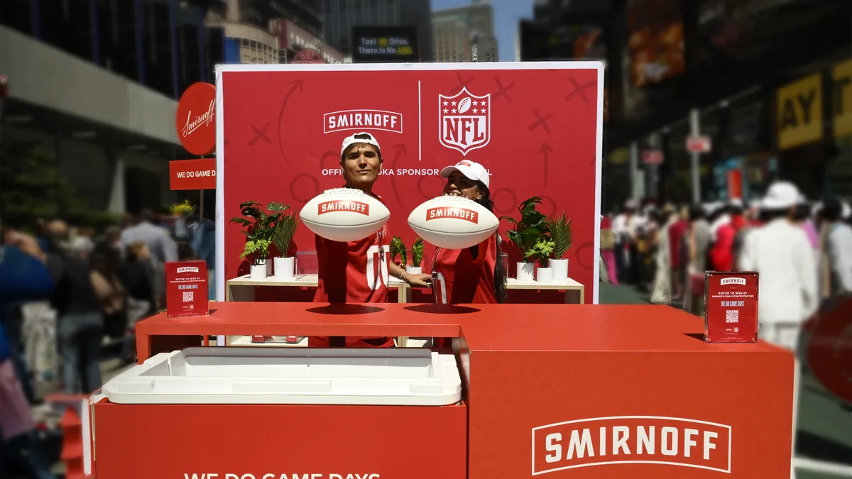 Two people hold footballs behind a red Smirnoff popup.