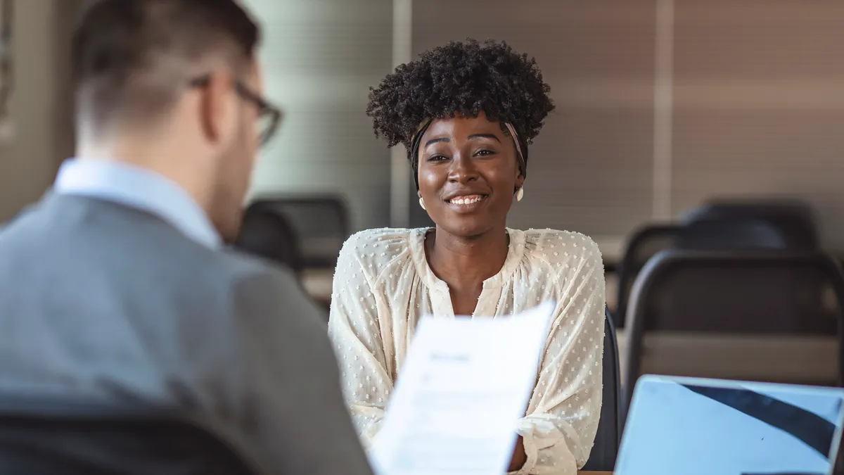 Person smiling and holding resume, sitting in front of businessman during meeting or job interview