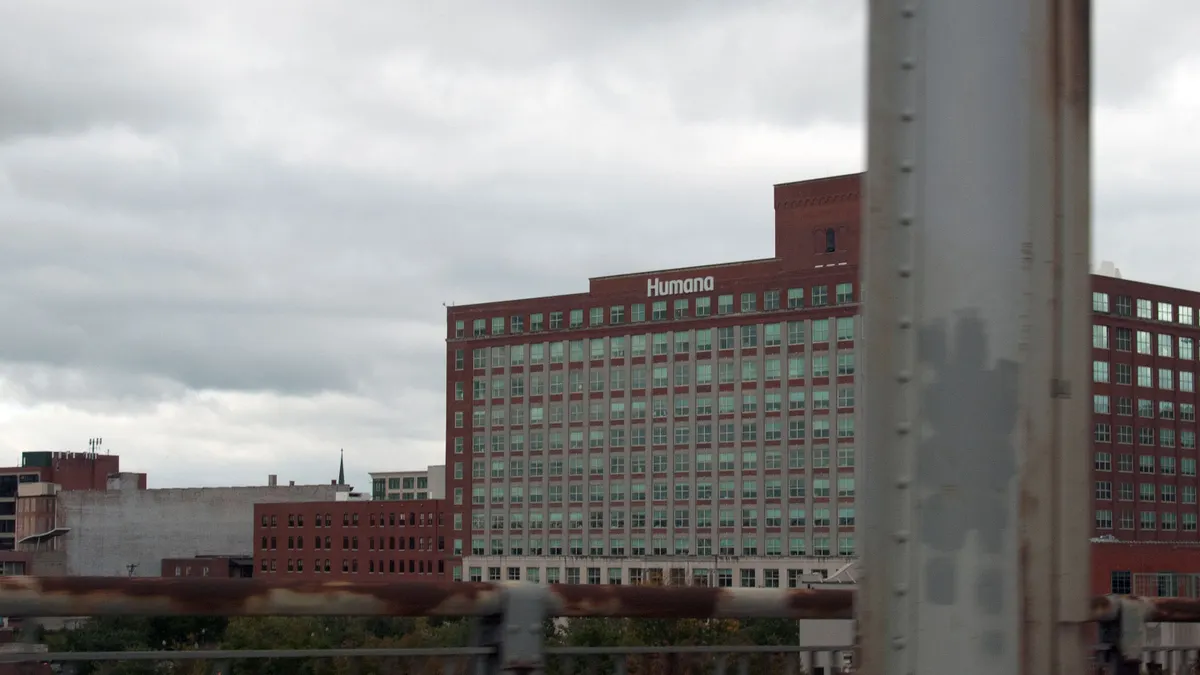A red-brick mid-rise office building with rows of windows and a “Humana” sign on the roof, seen under a cloudy gray sky.
