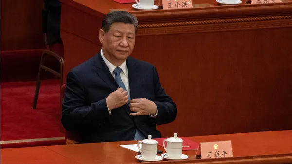 China President Xi Jinping sits at a table with two mugs in front of him.