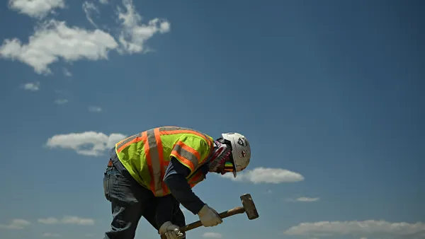 A construction worker swinging a sledgehammer during a sunny day.