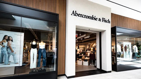 Storefront of Abercrombie & Fitch in a mall. Store windows on the left and right have mannequins wearing long pants and shirts.