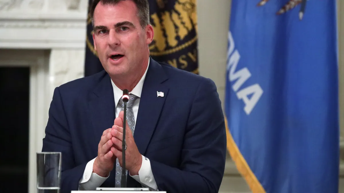 Oklahoma Governor Kevin Stitt speaks into a microphone with his hands clasped together