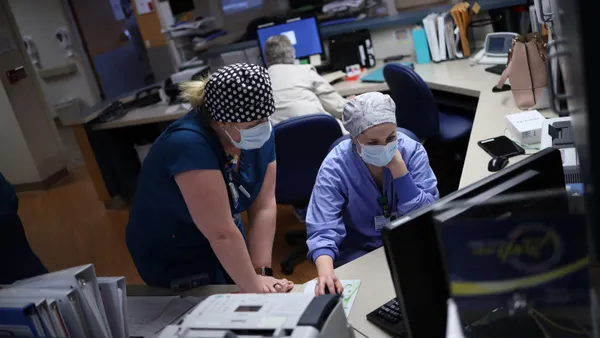 Nurses wearing surgical masks look at a computer in a hospital