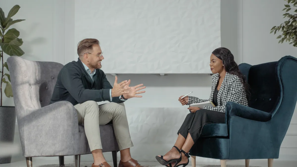 Two businesspeople sit across from each other in plush chairs, engaged and talking