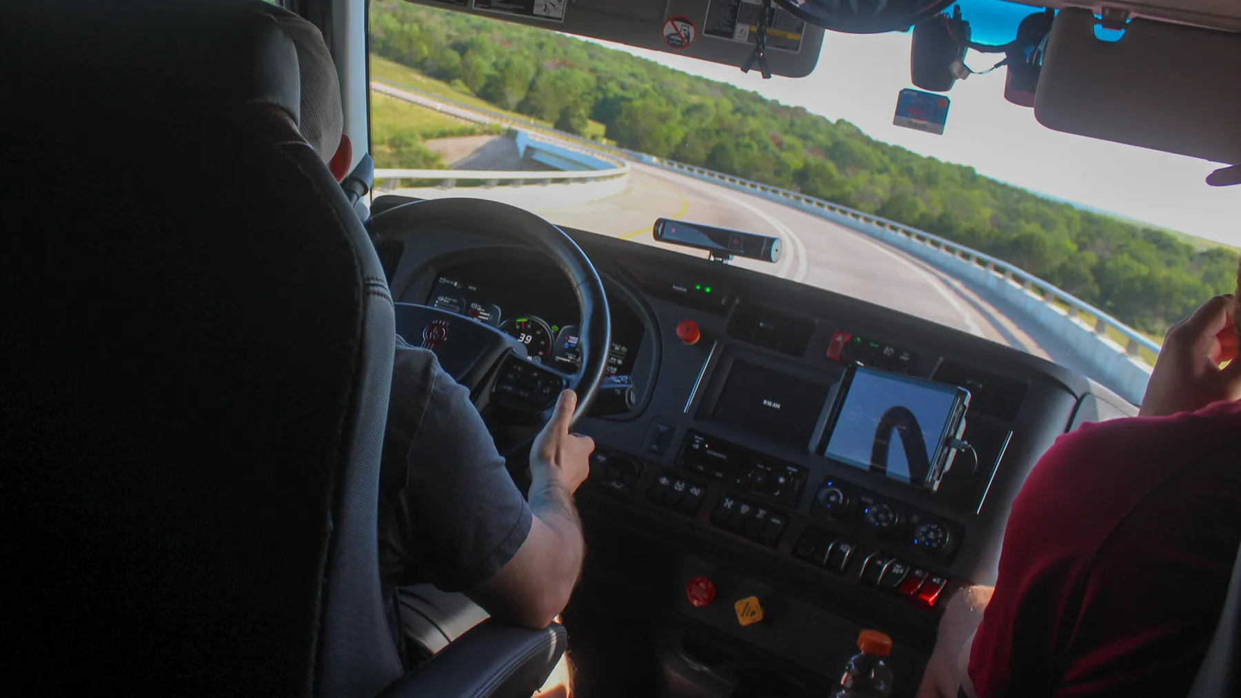 A safety driver monitors a self-driving Kodiak tractor-trailer navigate a turning ramp of a highway.