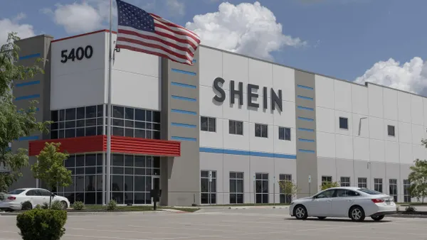 Modern distribution center for Shein with an American flag in front and a parking lot in the foreground, under a partly cloudy sky.