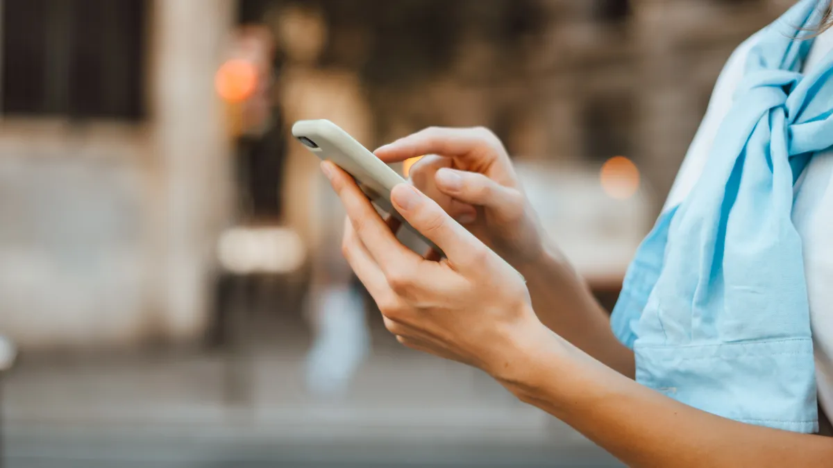 Close-up photo of female hands with smartphone. Young woman typing on a mobile phone on a sunny street.