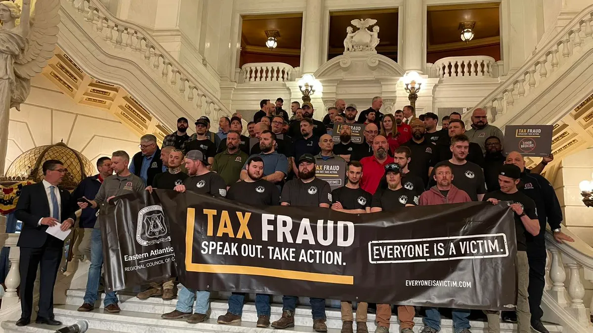 A group of people inside a government building pose on stairs and hold a sign protesting tax fraud.