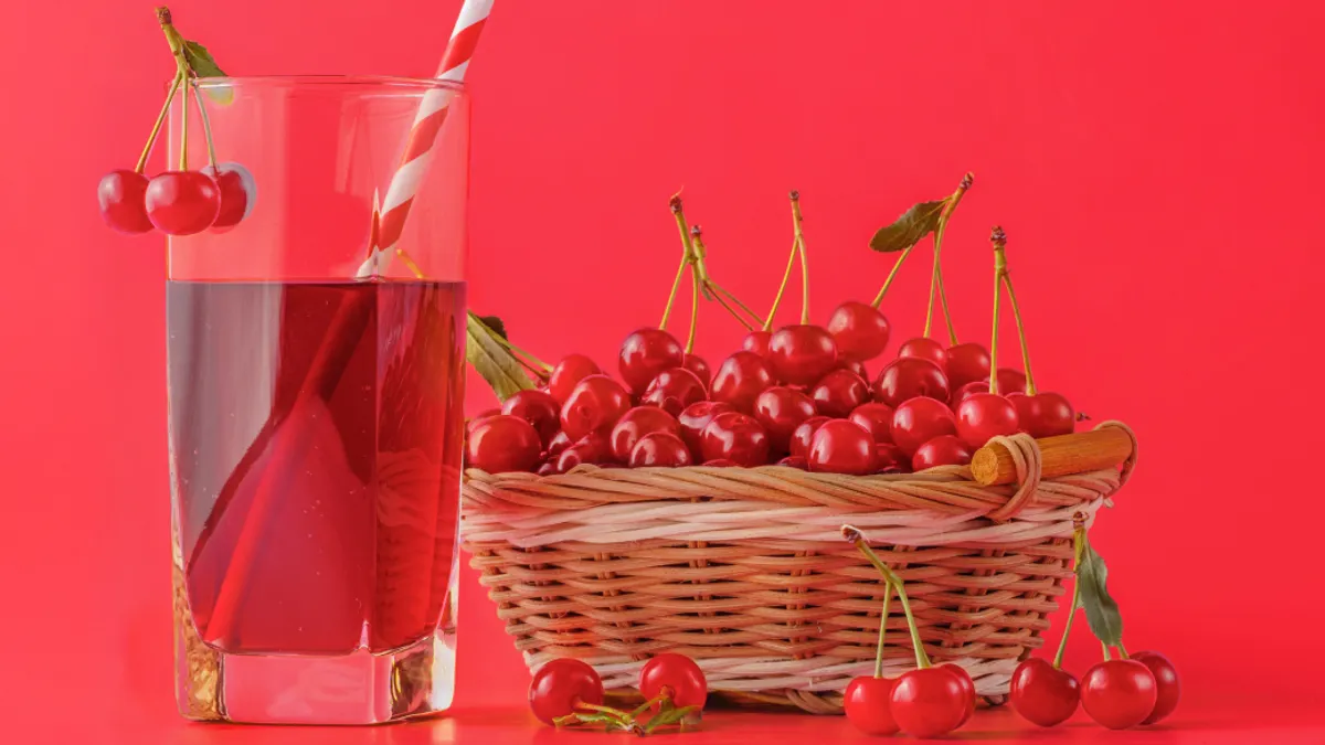 Basket of cherries and glass of juice with a red and white straw, garnished with cherries