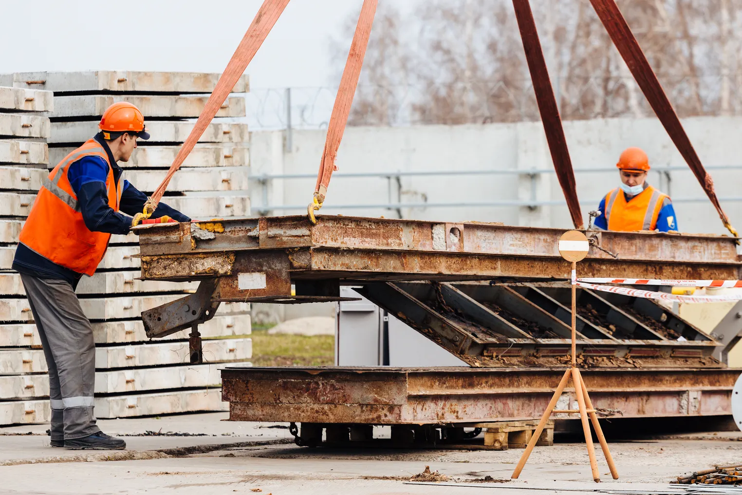 Slinger in helmet and vest controls unloading of metal structures on construction site.