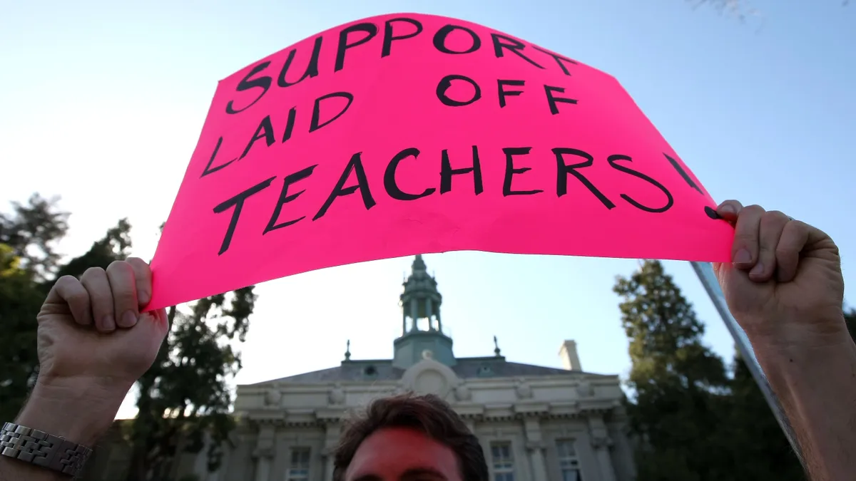 A demonstrator protesting teacher layoffs in Berkeley, California holds up a pink sign that reads "Support laid off teachers!"