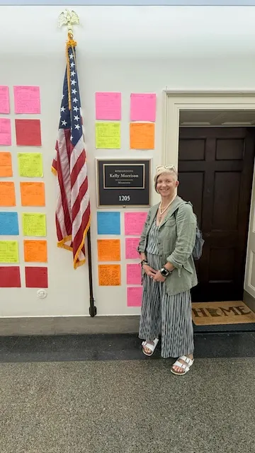 A person stands in front of an office door. There is a flag outside the door.