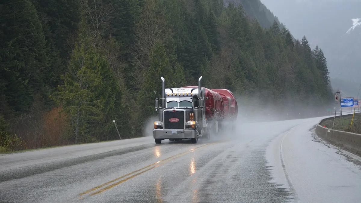 This is a truck on the highway. Also trees.