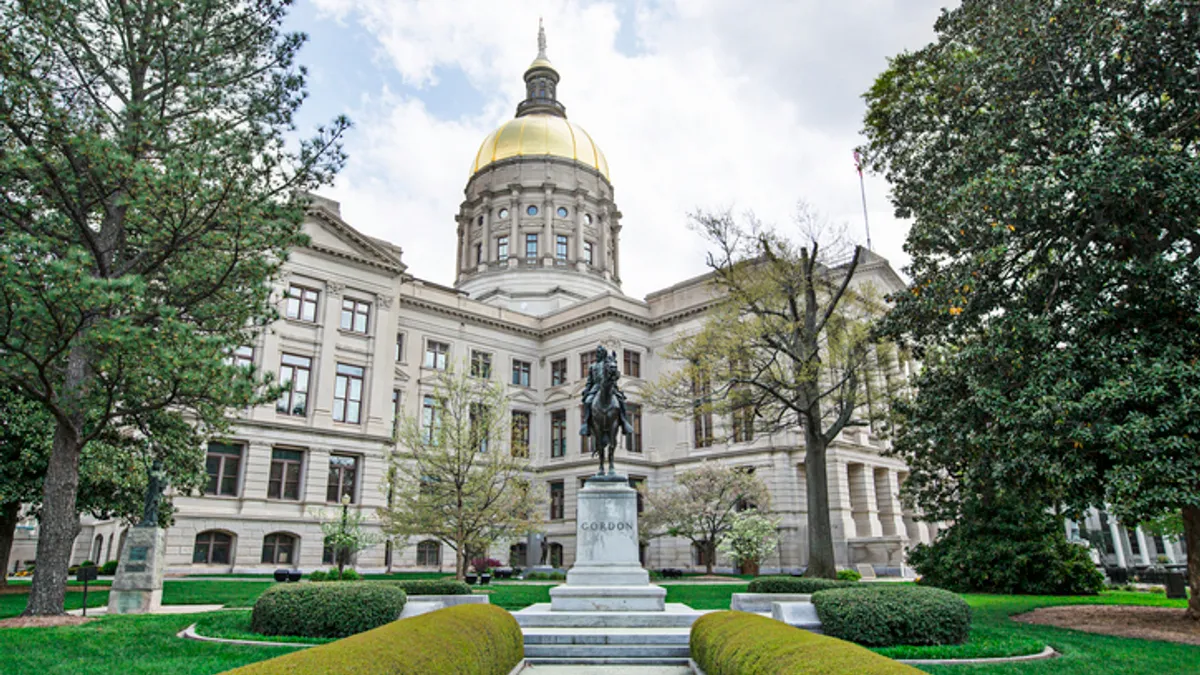 The outside of Georgia 's state capital is pictured. The facade is white and trees with green leaves surround the picture.