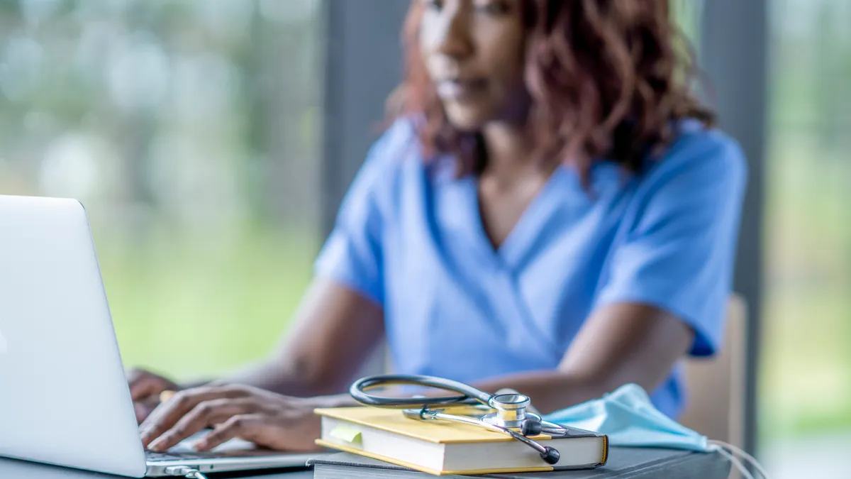 A woman wearing scrubs works at her laptop.