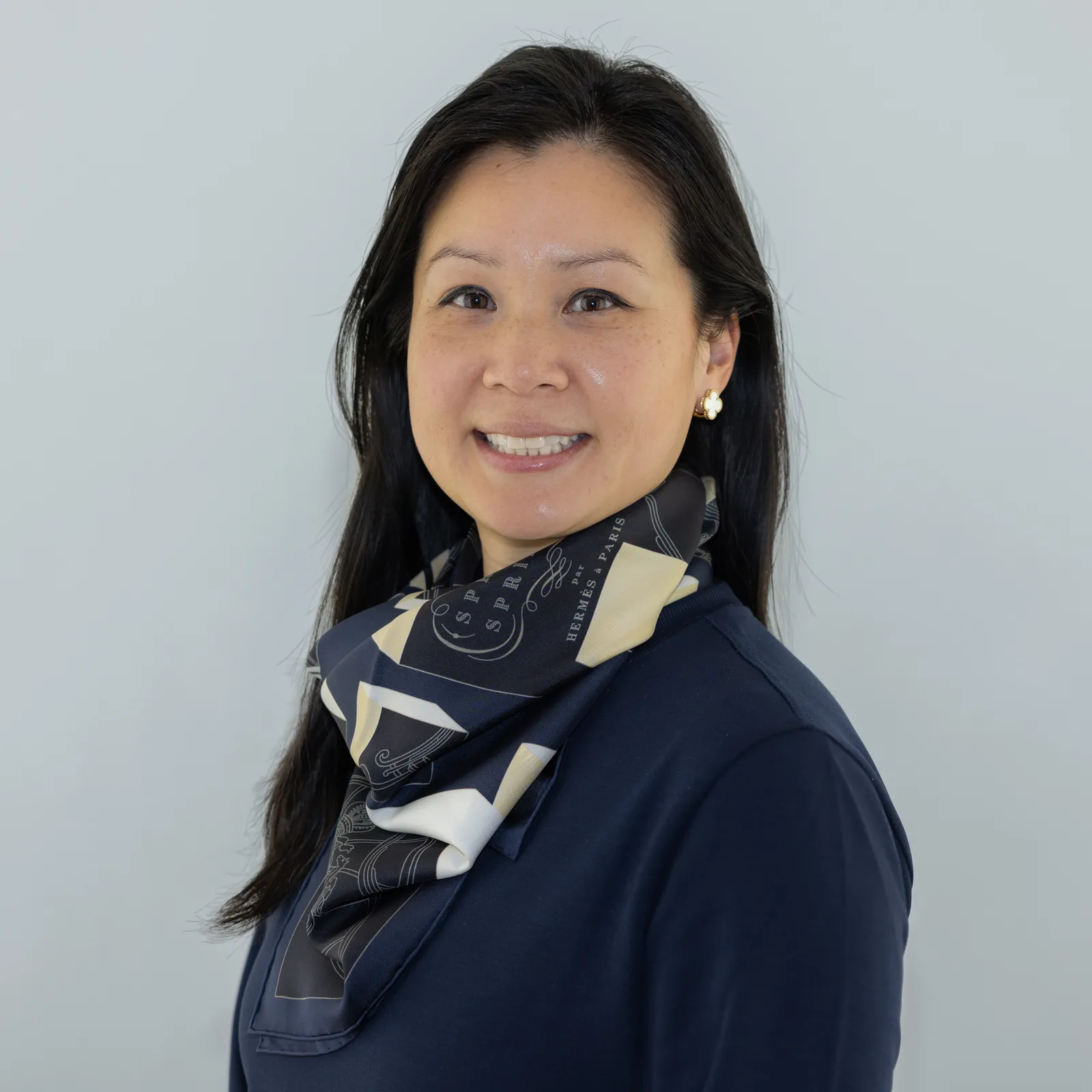 A woman with black hair in a dark blue shirt and scarf smiles at the camera.