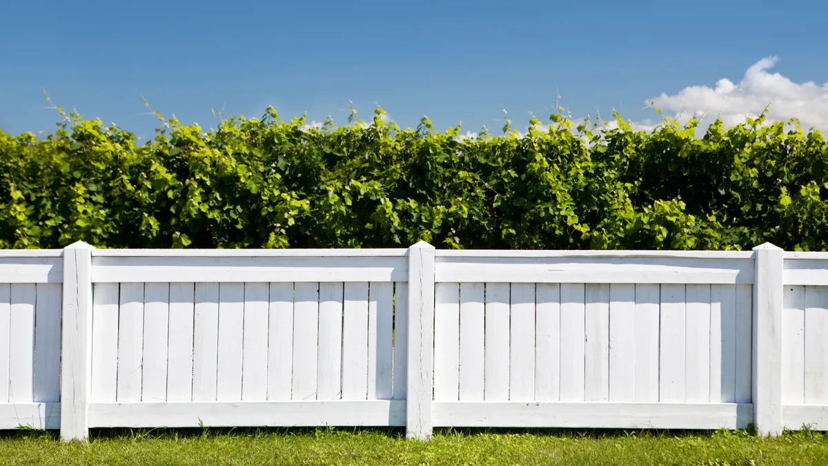 A white fence separates two yards.