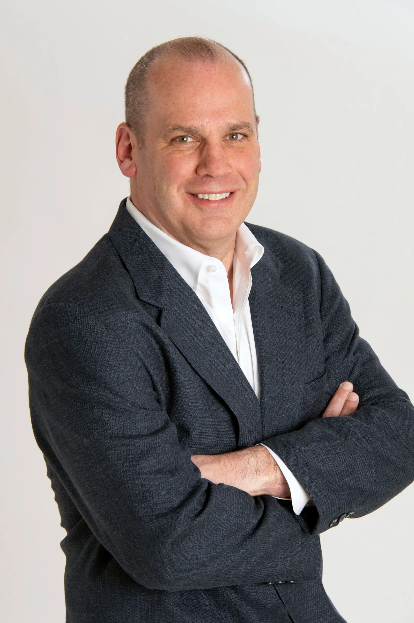 A person wearing a dark suit jacket smiles for a photo with their arms crossed.