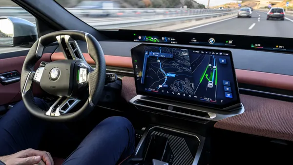 A human rides in the driver's seat of a new BMW iX3 50 xDrive, which is equipped with automated driving via the BMW Highway/Motorway-Assistant.
